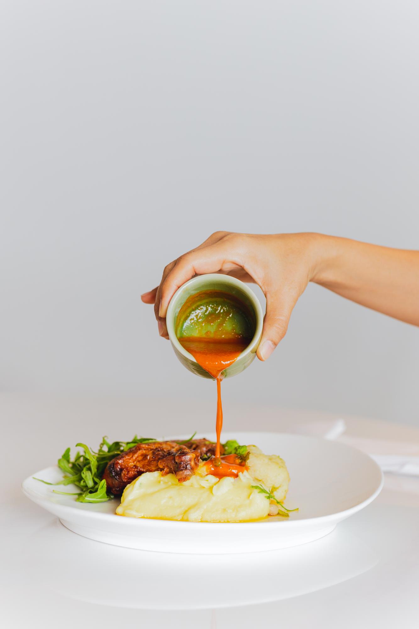 tight shot of hands finishing a plate with sauce